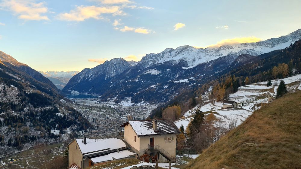 Foreground: a house. Background: a valley with a tiny-looking town, mountains on either side.