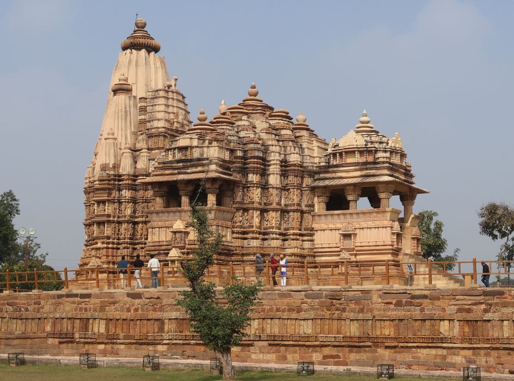 A large stone temple on a high platform with lots of ornate carvings covering its surfaces and a large stupa at one end.