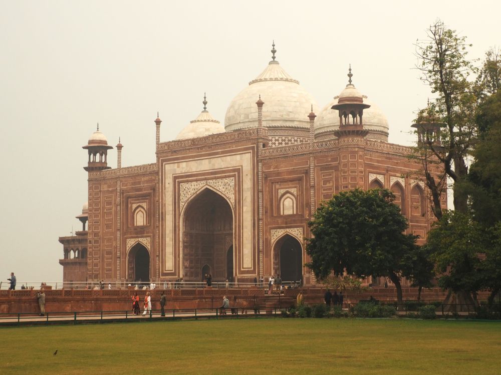 A large red sandstone building with white decoration and white domes and a large archway in its center.