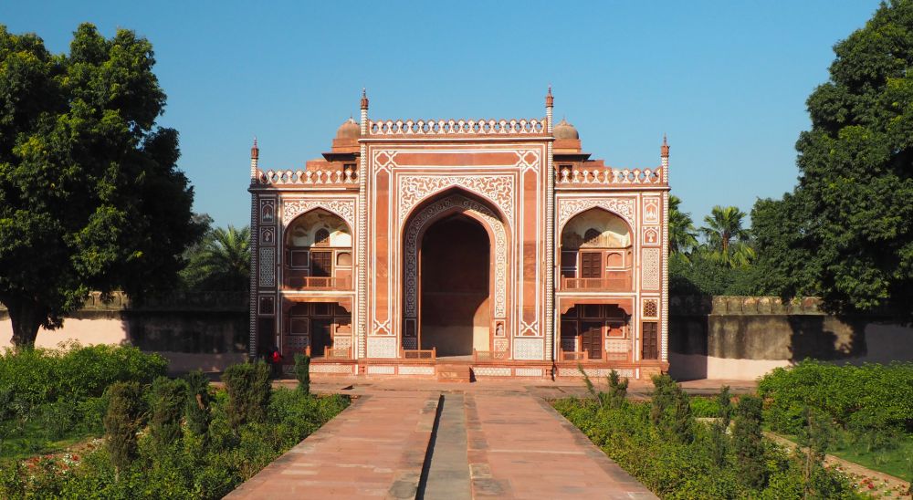 A red-sandstone building with a large archway in the center and white decorations all over.