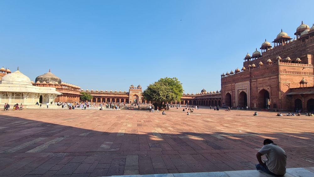 A huge courtyard, with a white building on the left and a larger red sandstone gateway on the right.