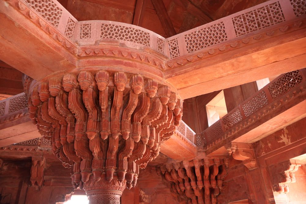 A very ornate column in the center of a room supporting beams radiating outwards to the sides of the room.