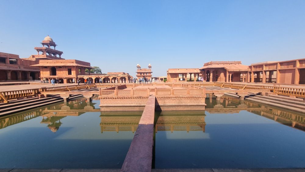 Scattered low red sandstone buildings and a small pool in front.