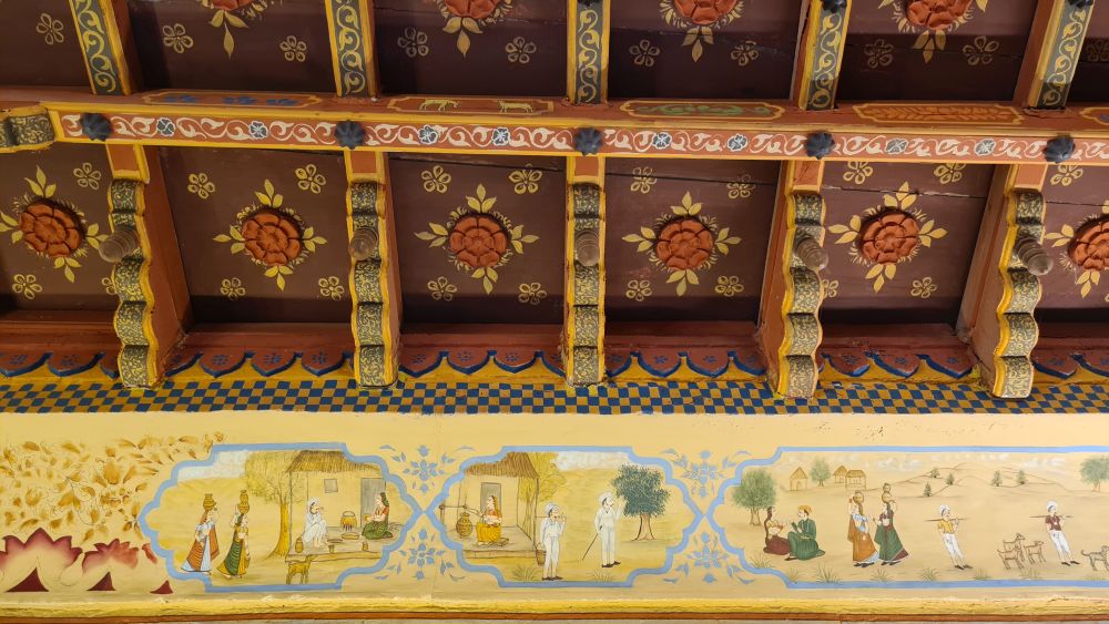 detail of a ceiling: carved with flowers and painted with scenes from stories.