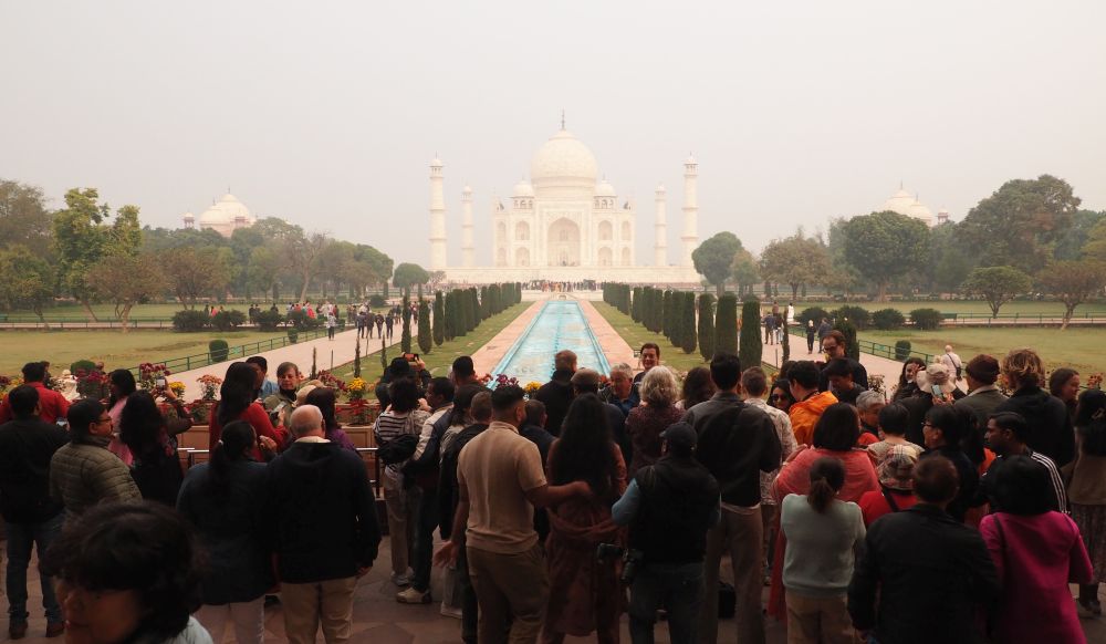 Int he foreground, a crowd of people, backs to the camera. In the background, the Taj Mahal.