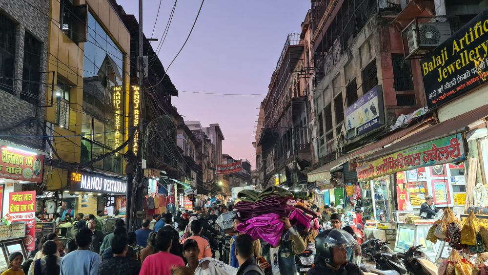 A very crowded street in the evening with brightly lit shops on either side and lots of pedestrians filling the street.