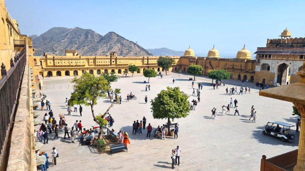 Looking from a bit above at a large courtyard with a scattering of people and high walls around it.