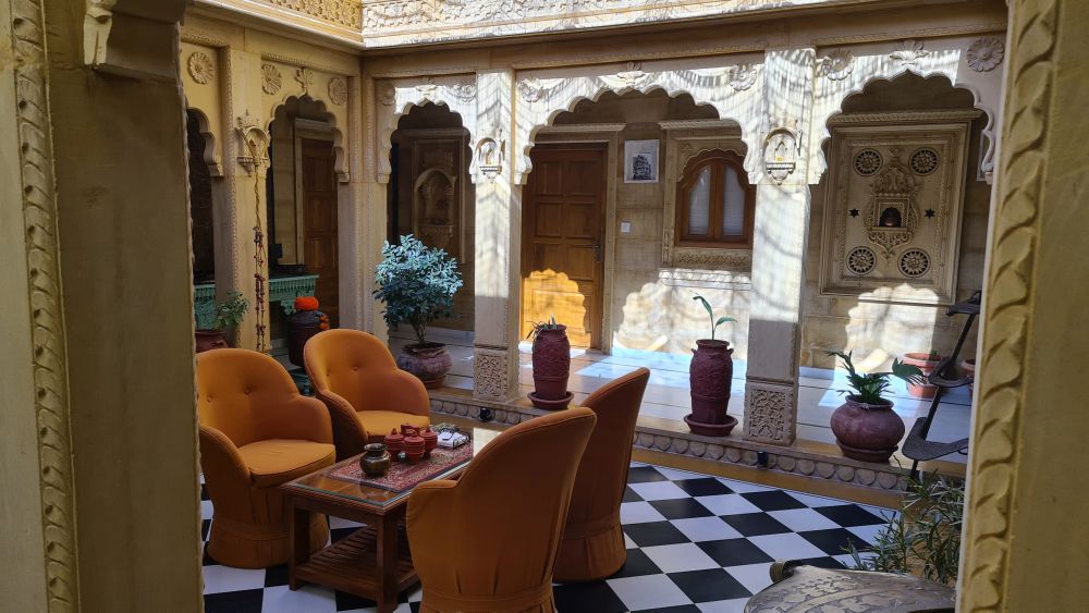 A courtyard with seats and a low table and detailed stonework on the pillars around it.