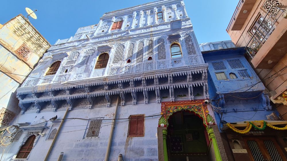 A light blue building of three stories with lots of decorative balcony stonework.