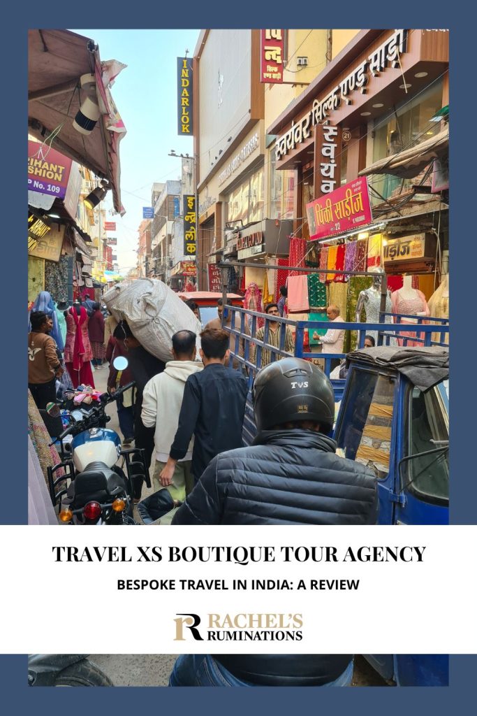 Text: Travel XS Boutique Tour Agency: Bespoke travel in India: a review. Image: a very crowded and narrow street with shops on both sides.