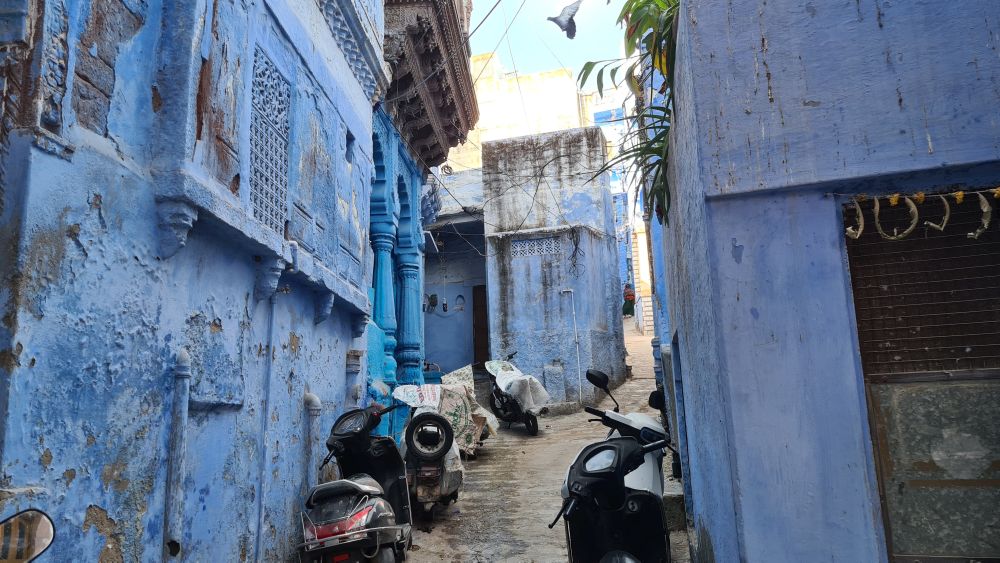 A narrow street with motorbikes parked along it. The buildings on both sides are blue.