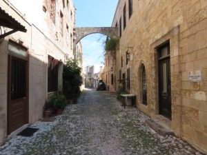 A narrow cobbled street with 2-3 story stone houses on either side.