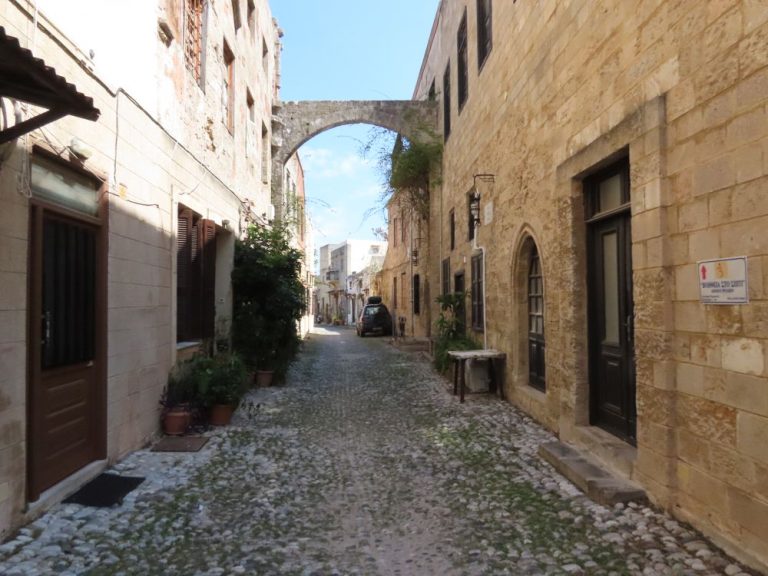 A narrow cobbled street with 2-3 story stone houses on either side.