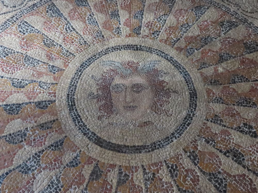 A mosaic floor shows a circle with the face of Medusa and a decorative pattern around the circle.