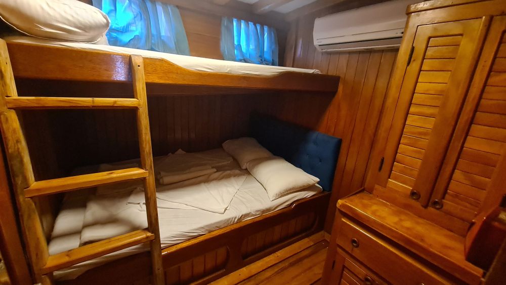 Wood-paneled, cupboard on the right, bunk bed against the wall, 2 windows above the upper bunk.