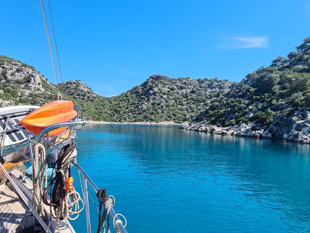 Calm blue water surrounded by hilly terrain: rocky with shrubs.