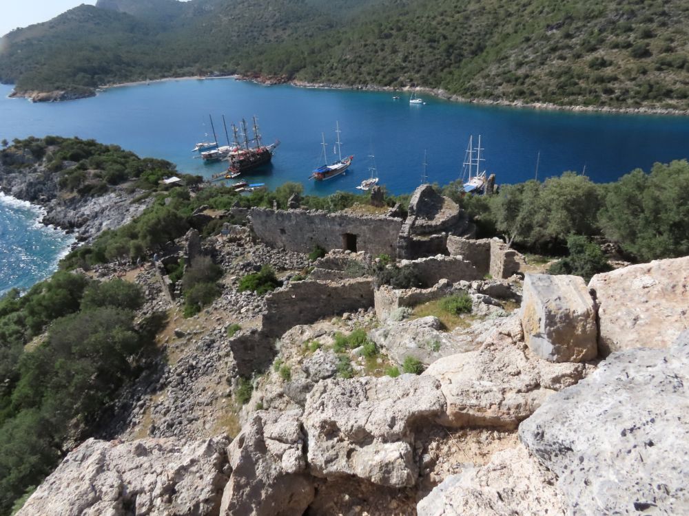 A view down to the bay where several boats are anchored. In the foreground, various ruins.