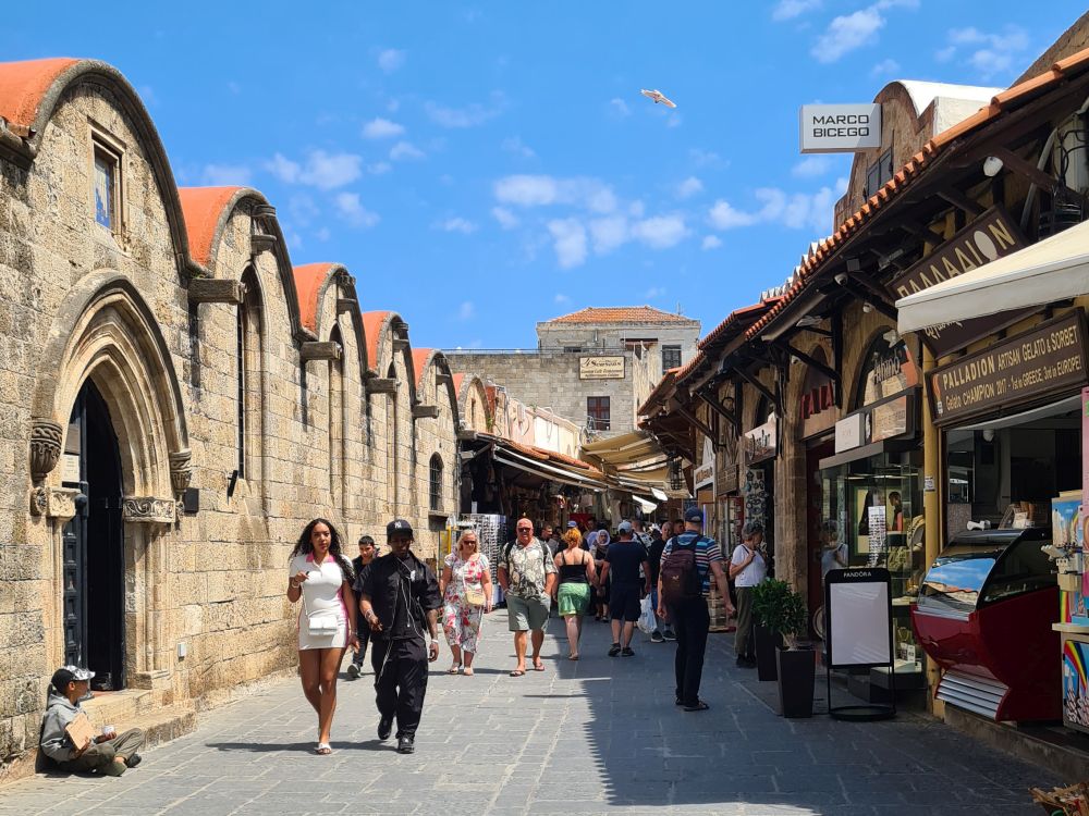A pedestrian street with shops on the right and a single-story building with a series of arched roofs on the left.