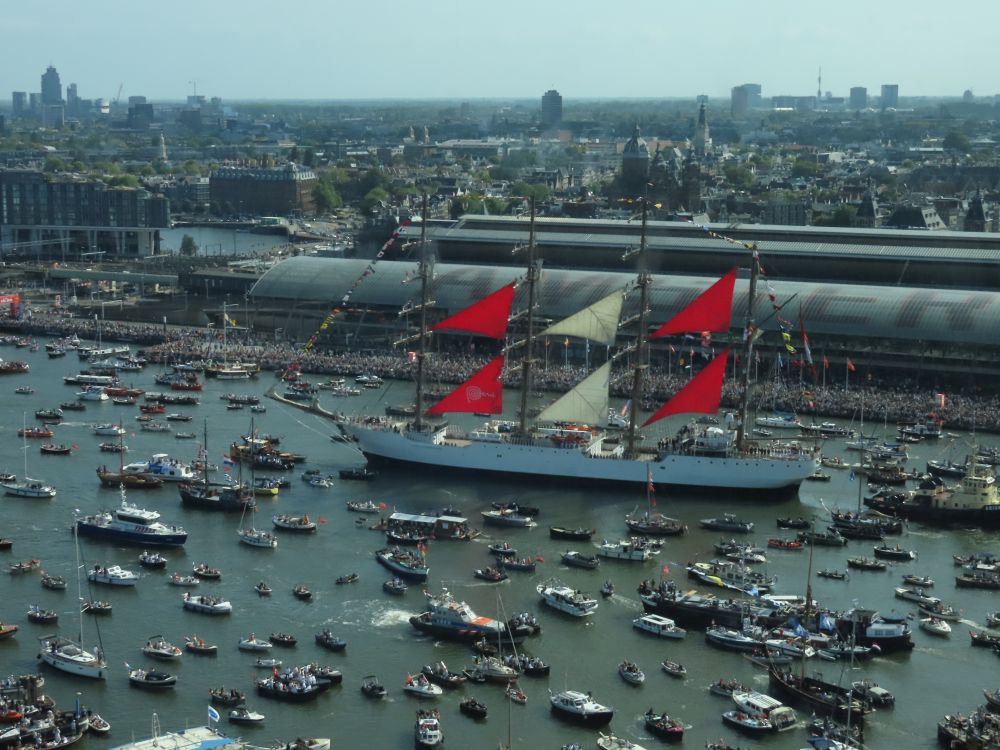 The water is covered with boats: one large ship with sails raised and lots of smaller ones.