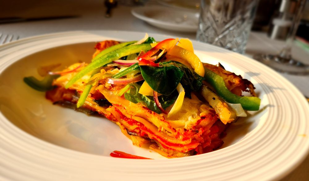 Lasagna on a white place with vegetables piled on top.