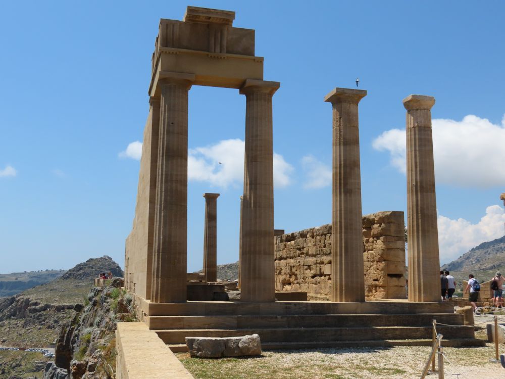 The temple has four columns along the front and solid sides, partially rebuilt.