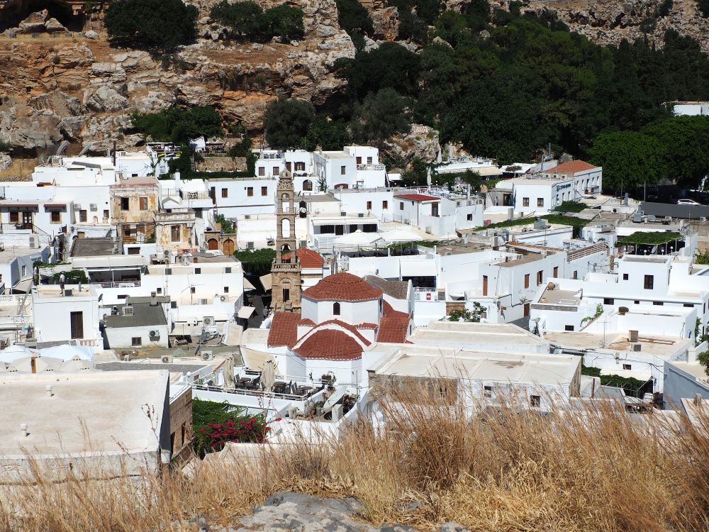 A cluster of white-washed houses, with a red-roofed church in the center with its tall stone belltower.