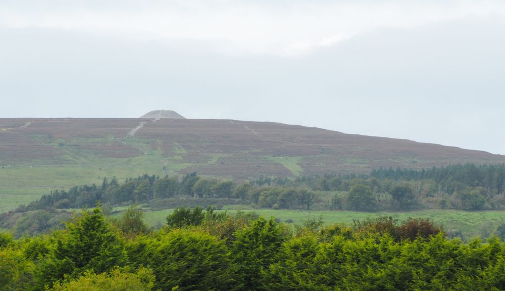 A large hill in the distance, with a cairn right at its top.
