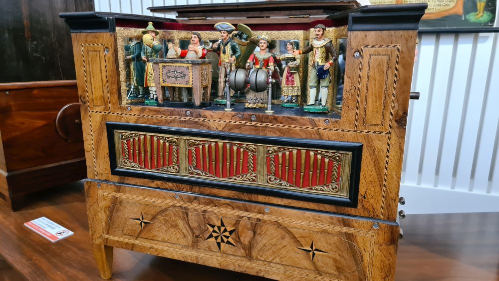 The organ is a square wooden box with inlays and a whole set of small figures portraying the band across its top.