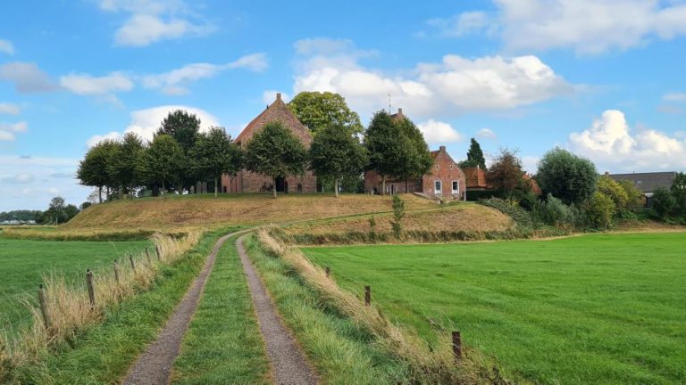 An unpaved road straight ahead through flat green pastures leads to a small, flat-topped mound with a church on it.