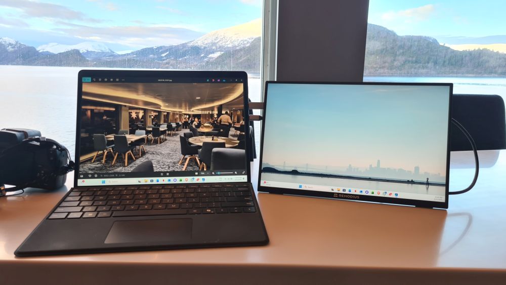 A Surface laptop on the left with a photo on its screen, the monitor on the right with a home screen showing a lot of sky.