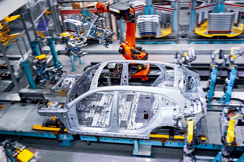 The skeleton of a car, with a big orange single-armed robot behind it.