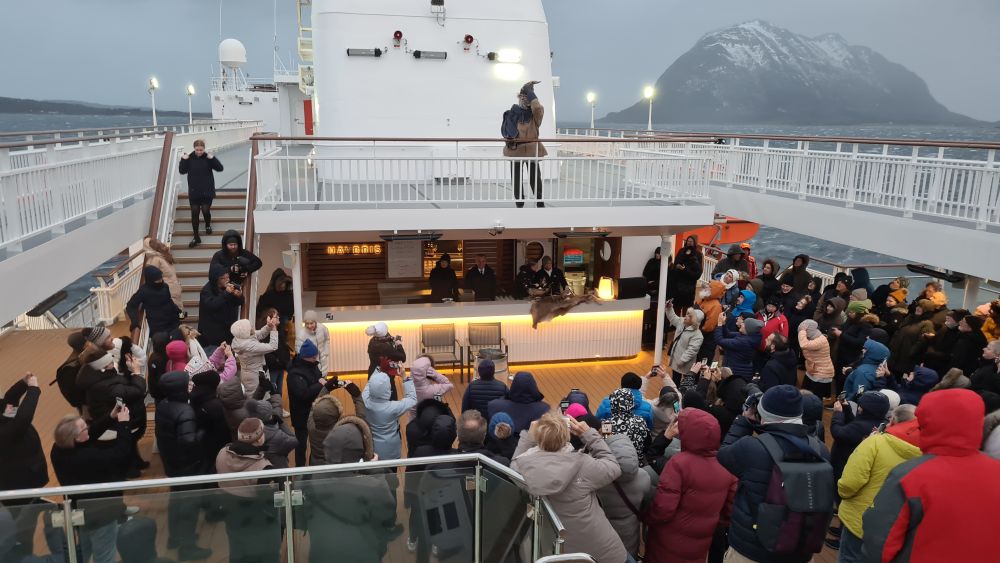 Seen from deck 9, a crowd of people, bundled in jackets and hats, stand with their backs to the camera. Njord stands above them on Deck 9.