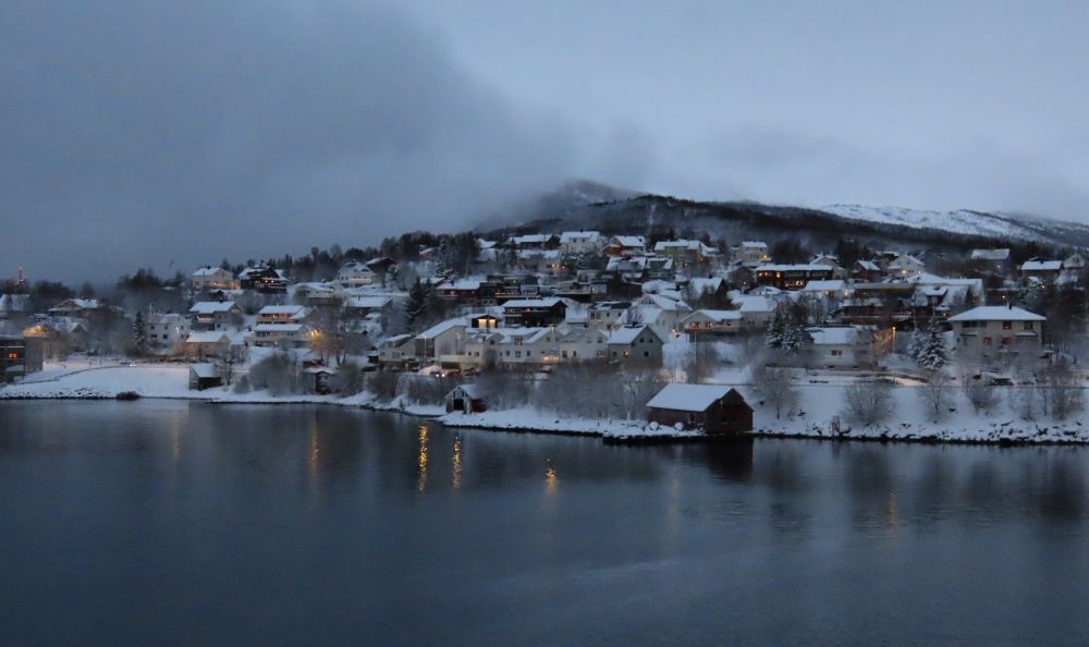 Clustered between water and a hill, a small, snow-covered village.