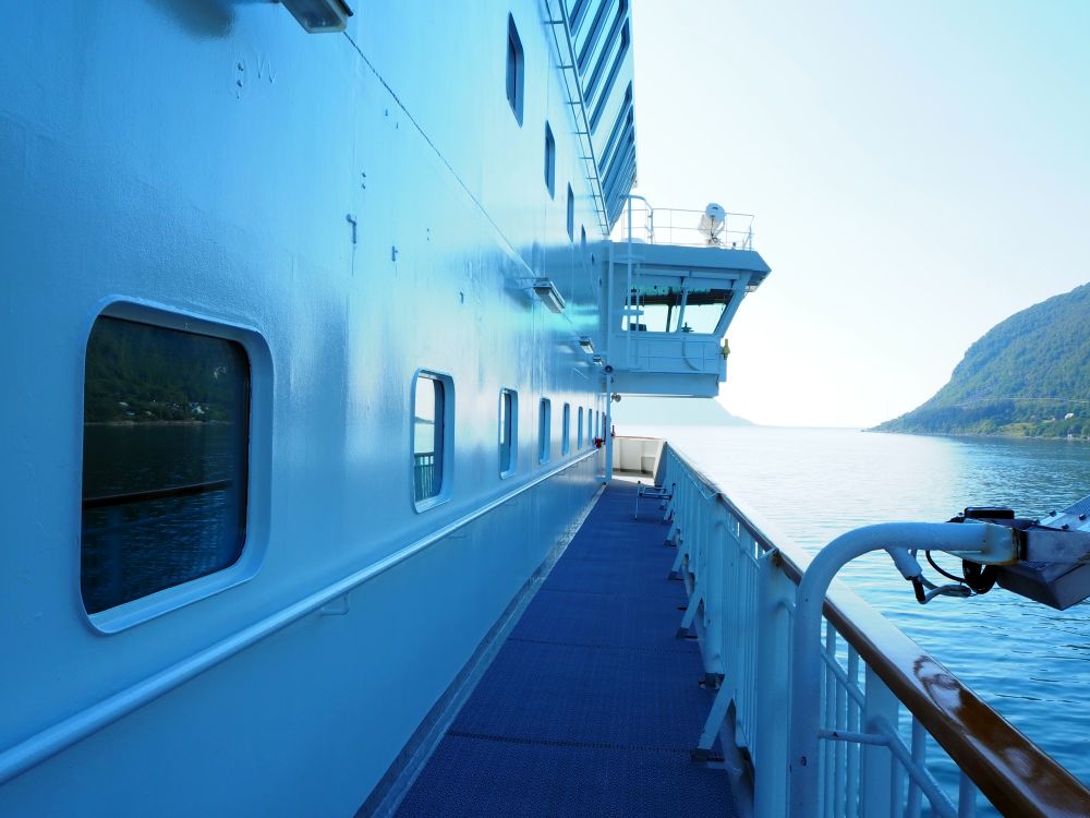 Looking down a walkway, a wall on the left with windows in it and a railing on the right.
