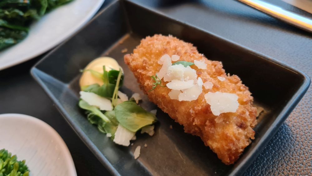 A single fried croquette with a sprinkle of cheese shavings on it.