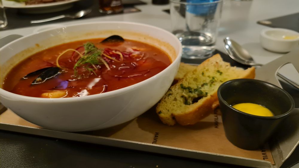 A bowl of soup with a buttered slice of bread beside it.