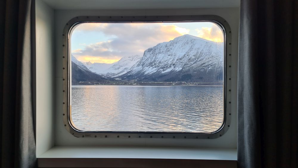 A rectangular window frames a view of a snow-covered mountain across an expanse of water.