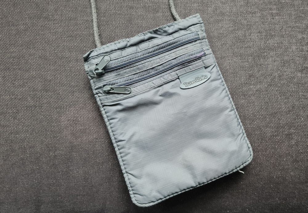 A grey passport wallet with a neck strap and 2 zipper pockets.