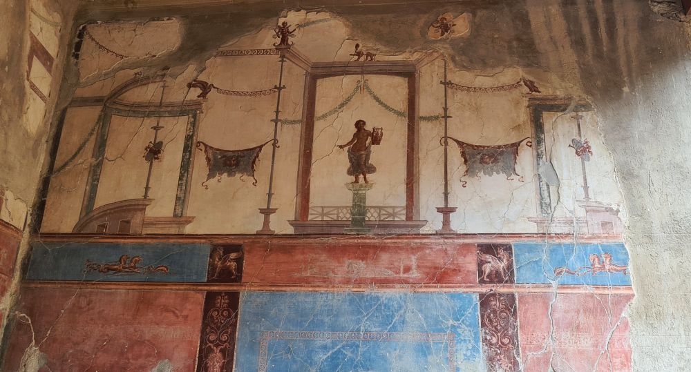 Blue and red symmetrical panels below, divided by images of columns. Above, on a white background, panels defined by detailed painted frames with small images within them.