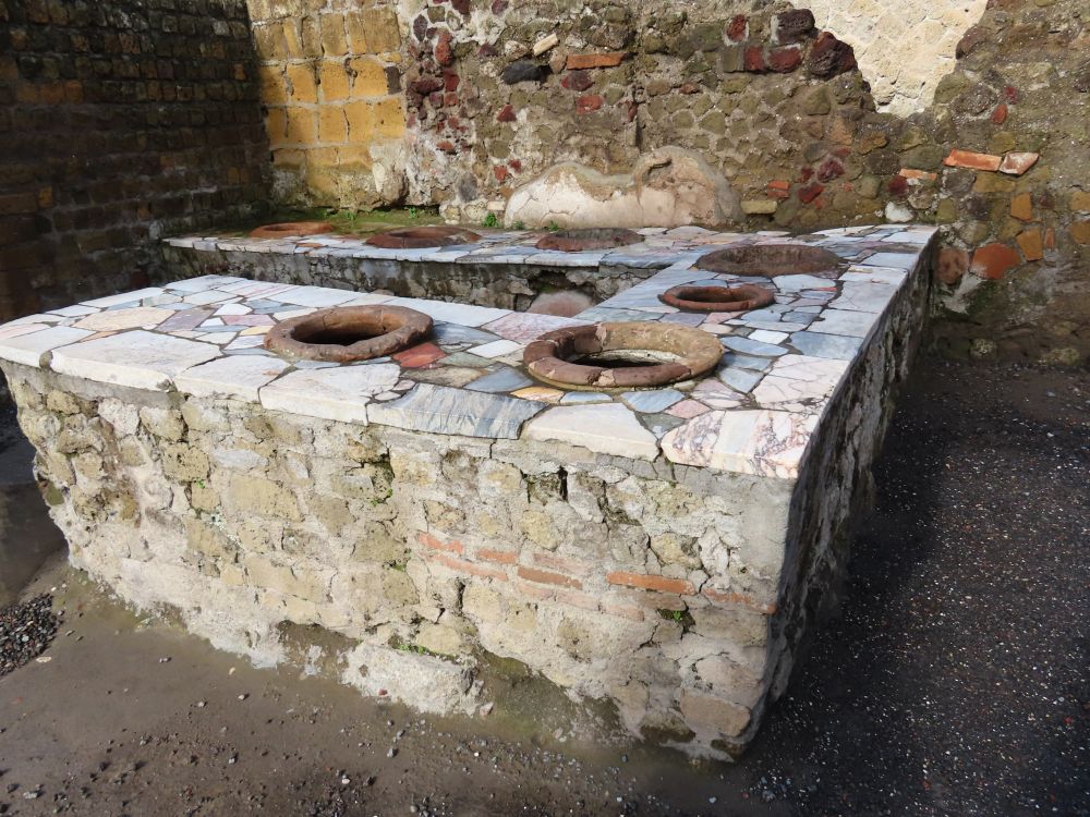 A counter in a U shape, covered in marble, with round holes along it, each with a terracotta clay edge.