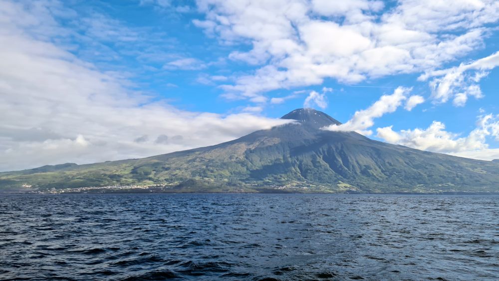An island with a huge volcanic mountain, with fluffy clouds around its peak.