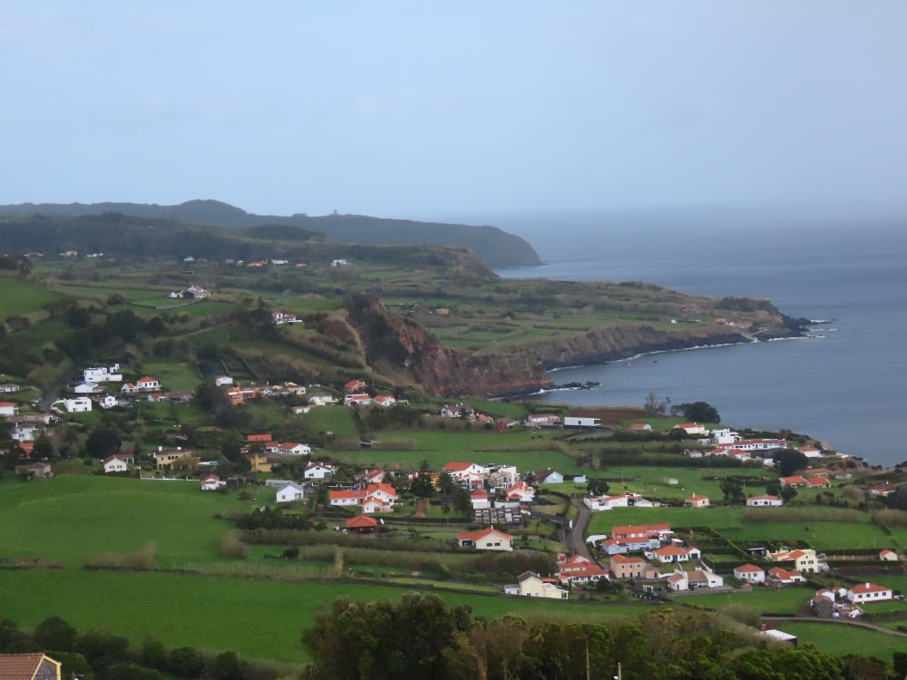 View over cliff-edged landscape, green fields, a white cluster of houses.