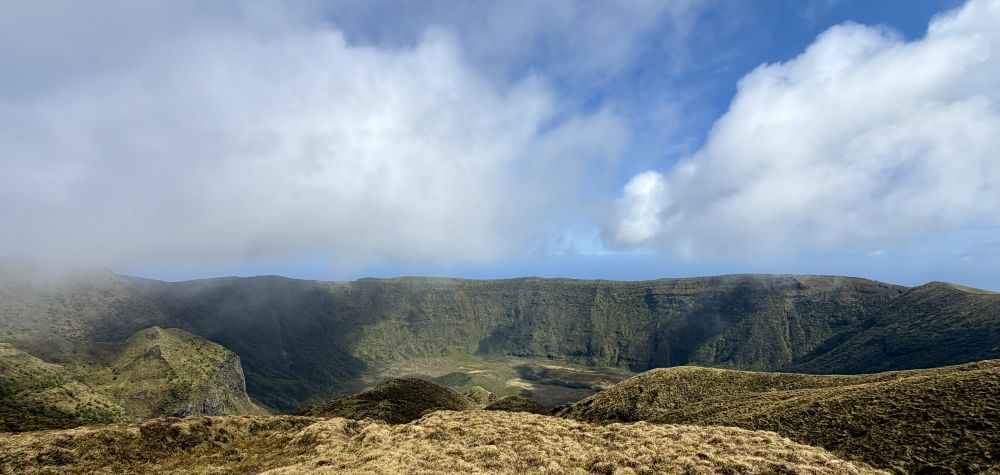 A view of grass-covered volcano crater seen from its edge.