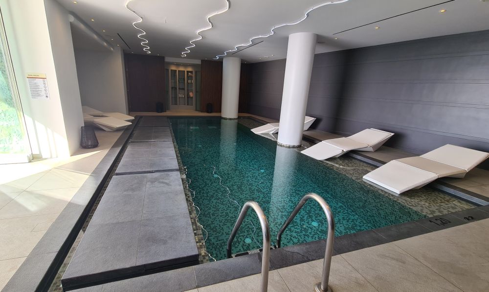 A small blue-tiled pool with loungers half in the shallow sides of the pool. Low ceiling.