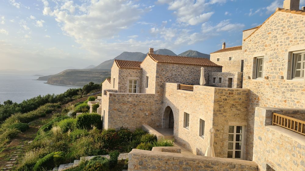 Stone buildings in the foreground, the hills of the coast and the sea in the background.