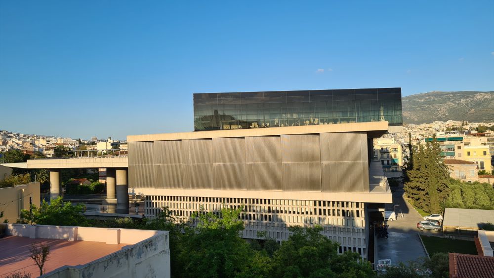 A big modern building of concrete with a top floor of glass.