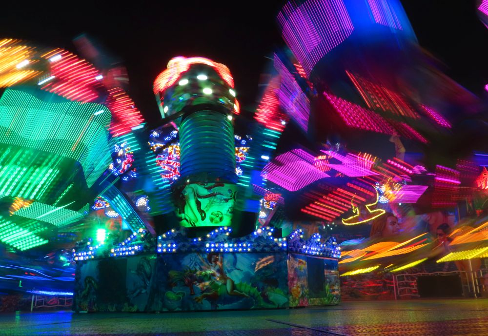 A ride lit in many colors at night - moving so fast all but the center axis is blurred.