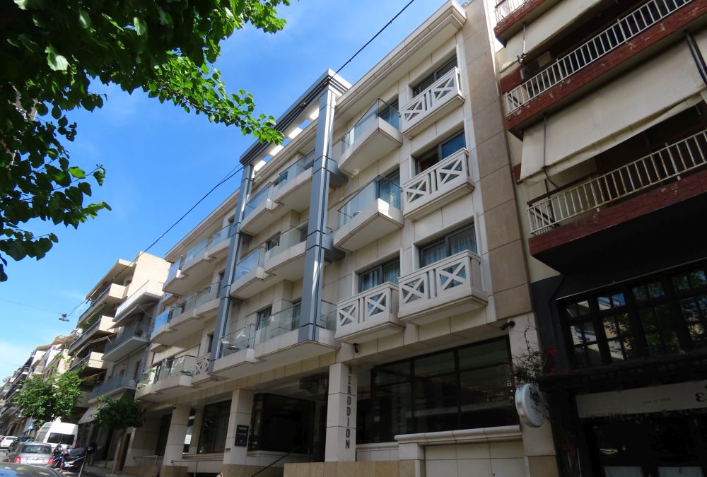 A white building of about 5 stories framed by other buildings of similar size.