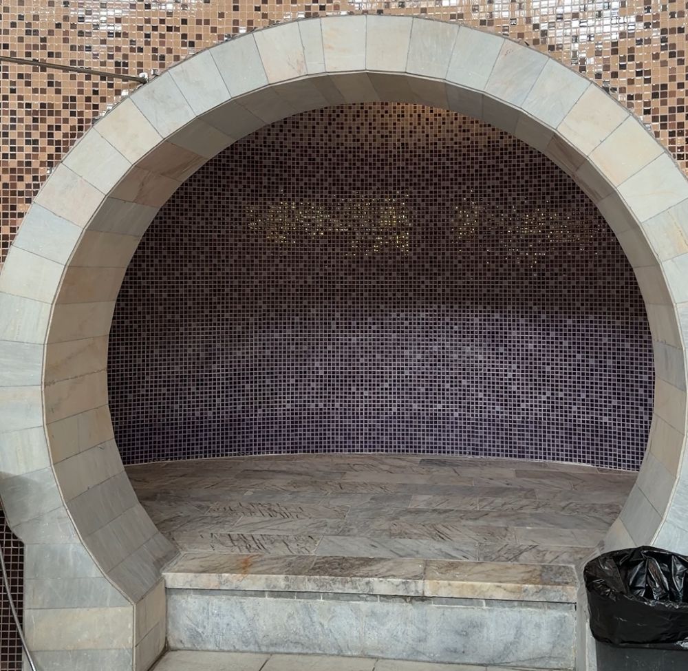 A round opening in a tiled wall - except for the flat floor - opens into an empty tiled space with rounded walls.