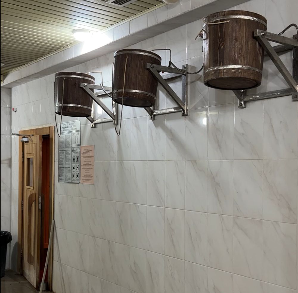 A marble-tiled wall with 3 wooden buckets up near the ceiling. Each has a rope hanging from it to enable tipping it.